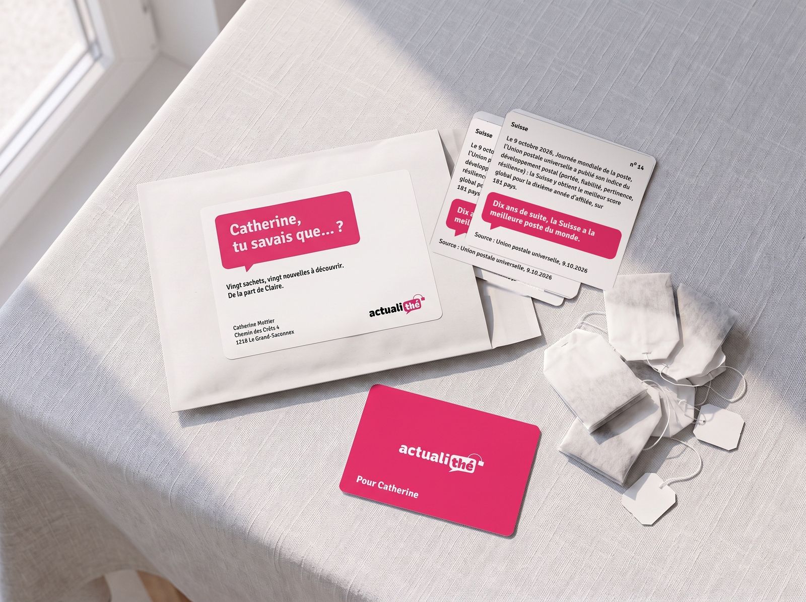 La pochette blanche avec son étiquette « Catherine, tu savais que… ? », des cartes d’actualité et des sachets de thé, posés sur une table.